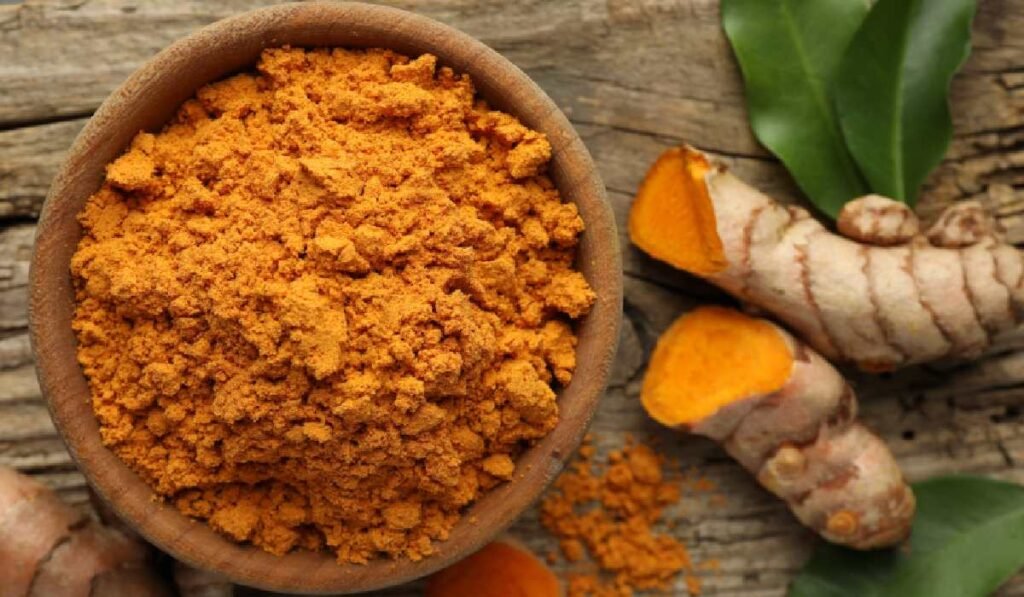 Pudră aromatică de turmeric și rădăcini crude pe masă de lemn