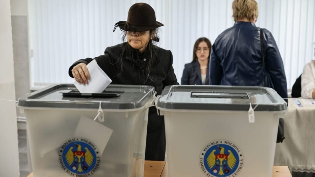 Mesajul lui Traian Băsescu, transmis înainte de alegerile din Republica Moldova: „O țară mică îi va administra o bătaie umilitoare lui Vladimir Putin” În prim-plan, o femeie în vârstă îmbrăcată în negru și cu o pălărie neagră care îi acoperă fața introduce buletinul de vot în urnă, după ce și-a exprimat opțiunea la alegerile parlamentare din Republica Moldova, iar în spate se mai văd câteva persoane, 28 septembrie 2025