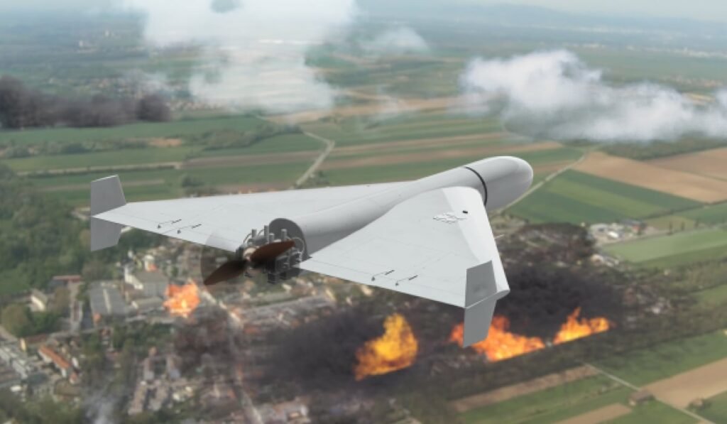 O dronă militară se află în zbor deasupra unei zone cu case și copaci. Două focare mari de incendiu sunt vizibile în peisaj, unul în partea din față a imaginii și celălalt în partea stângă, mai în spate.