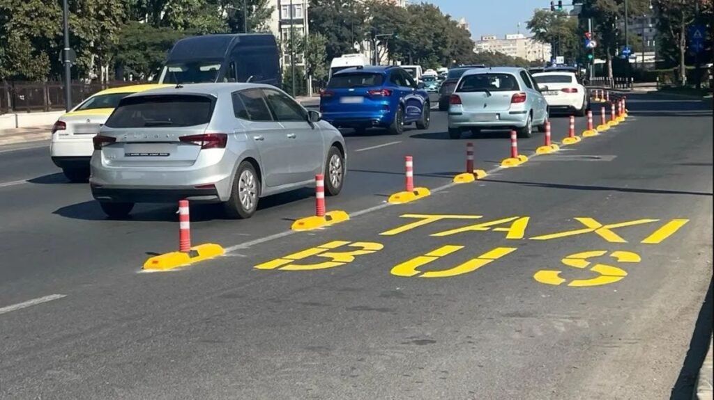 În partea stângă, mai multe mașini circulă pe bulevard, iar în dreapta se vede o zonă lată, delimitată de stâlpișori și pe care scrie cu vopsea galbenă Taxi Bus, în Constanța, septembrie 2025